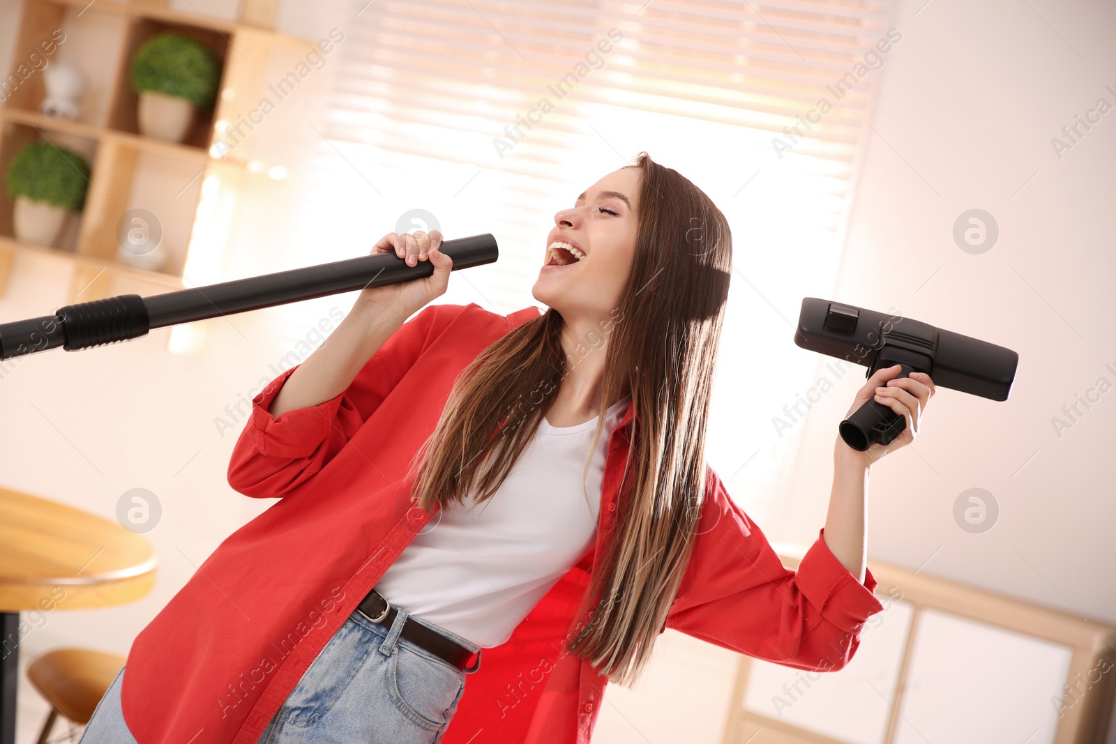 Photo of Young woman having fun while vacuuming at home