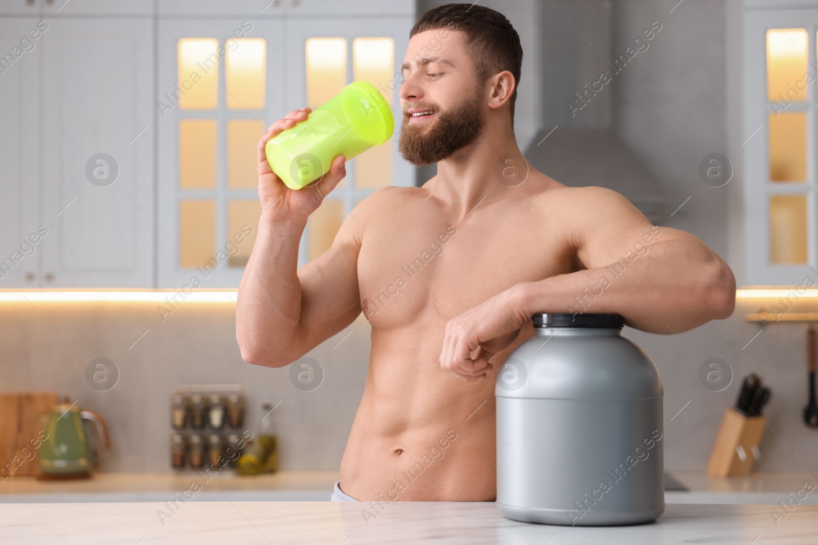 Photo of Young man with shaker of protein and powder at white marble table in kitchen