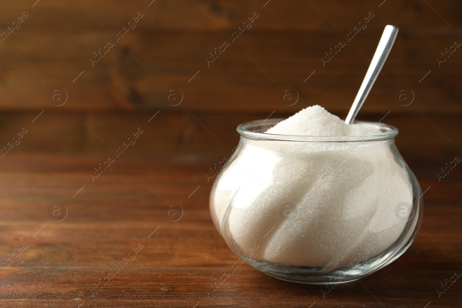 Photo of Glass bowl with sugar and spoon on wooden table. Space for text