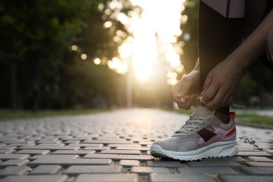 Photo of Woman tying shoelaces before morning run in park, closeup. Space for text