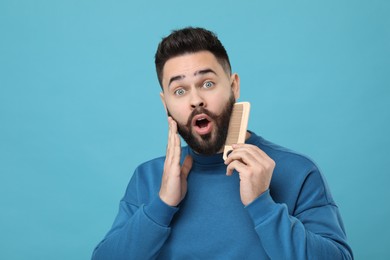 Photo of Surprised young man combing beard on light blue background