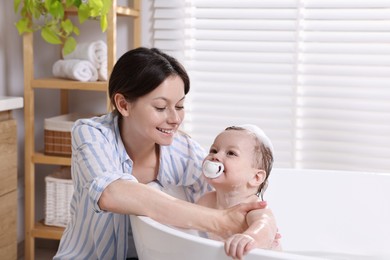 Mother bathing her cute little baby in tub at home