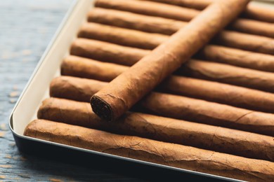 Photo of Many cigars in box on grey wooden table, closeup