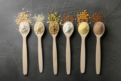 Spoons with different types of flour and ingredients on grey background, top view