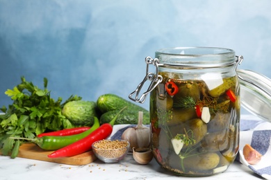 Photo of Jar with pickled cucumbers on marble table against blue background, space for text