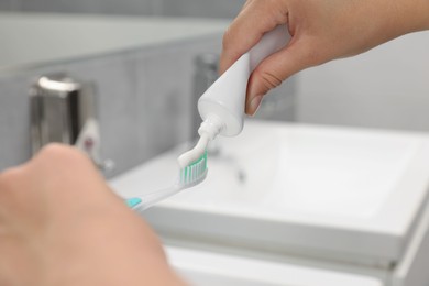 Woman applying toothpaste on brush in bathroom, closeup