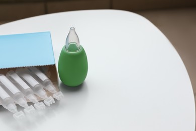 Photo of Package with single dose ampoules of sterile isotonic sea water solution and nasal aspirator on white table. Space for text