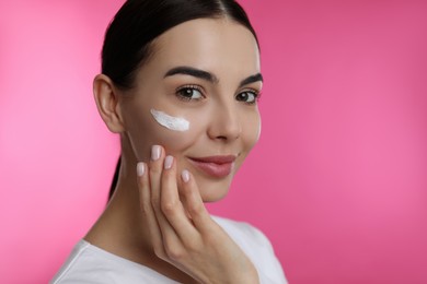 Photo of Young woman applying facial cream on pink background
