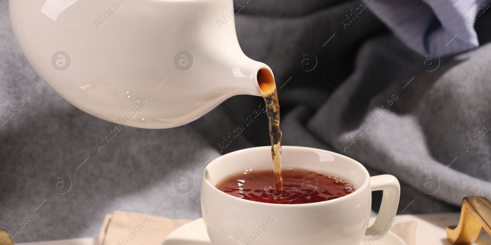 Photo of Pouring aromatic tea into cup in bed, closeup