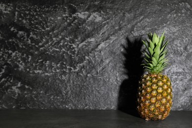 Photo of Whole ripe pineapple on grey table near black wall, space for text