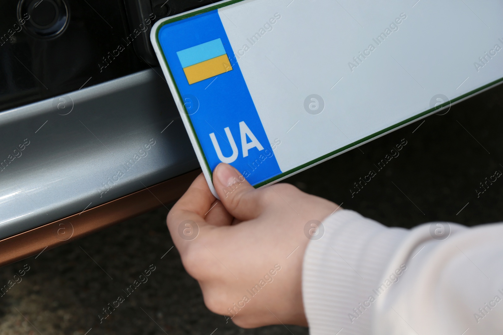 Photo of Woman installing vehicle registration plate outdoors, closeup