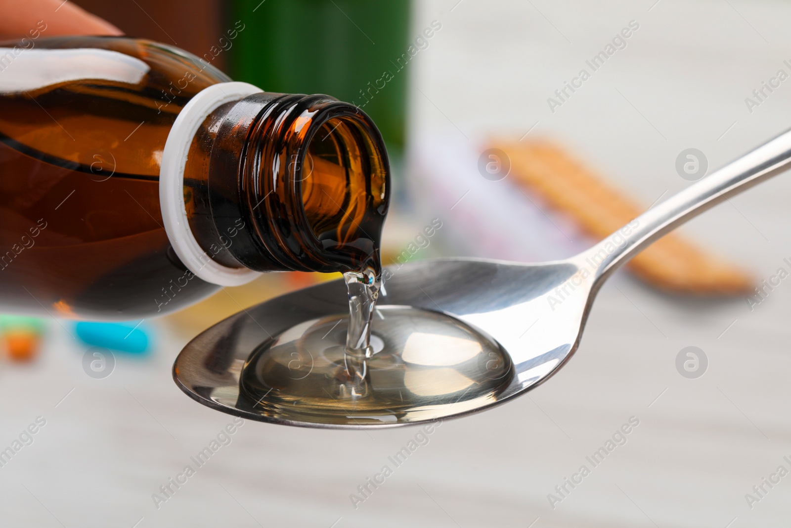 Photo of Pouring syrup from bottle into spoon against blurred background, closeup. Cold medicine