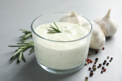 Photo of Fresh garlic bulbs, bowl of sauce, rosemary and pepper on grey background, closeup