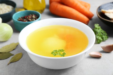 Delicious chicken bouillon and ingredients on light grey textured table, closeup