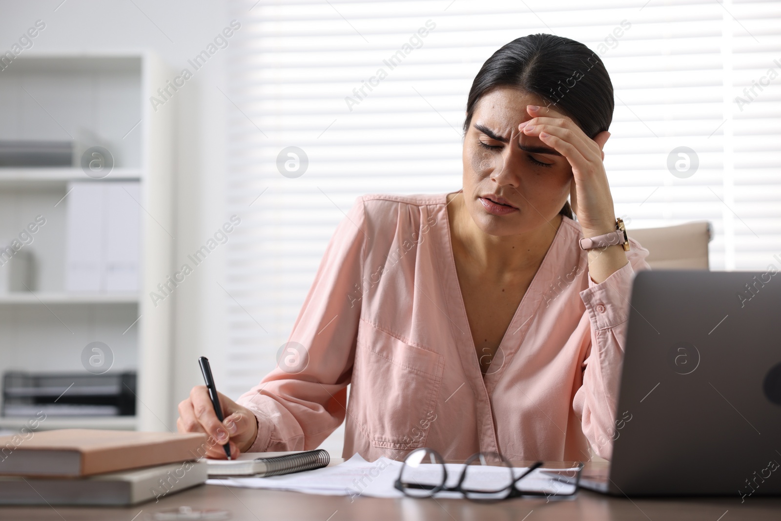 Photo of Young woman suffering from headache at wooden table in office