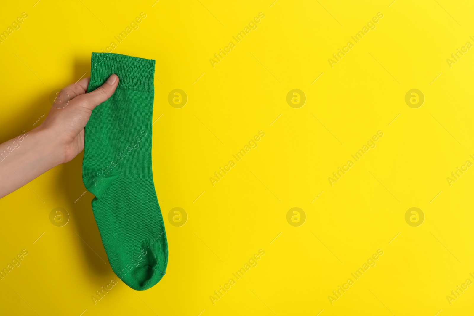 Photo of Woman holding green sock on yellow background, closeup. Space for text