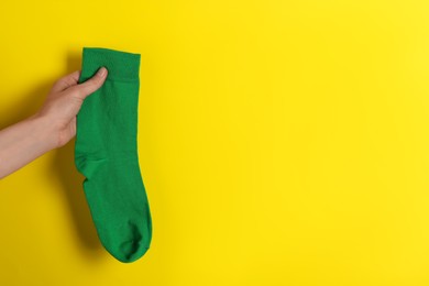 Woman holding green sock on yellow background, closeup. Space for text