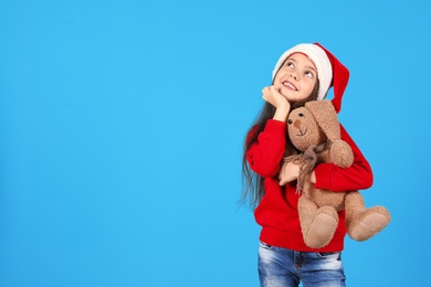 Photo of Cute little child in Santa hat with toy rabbit on color background. Christmas celebration