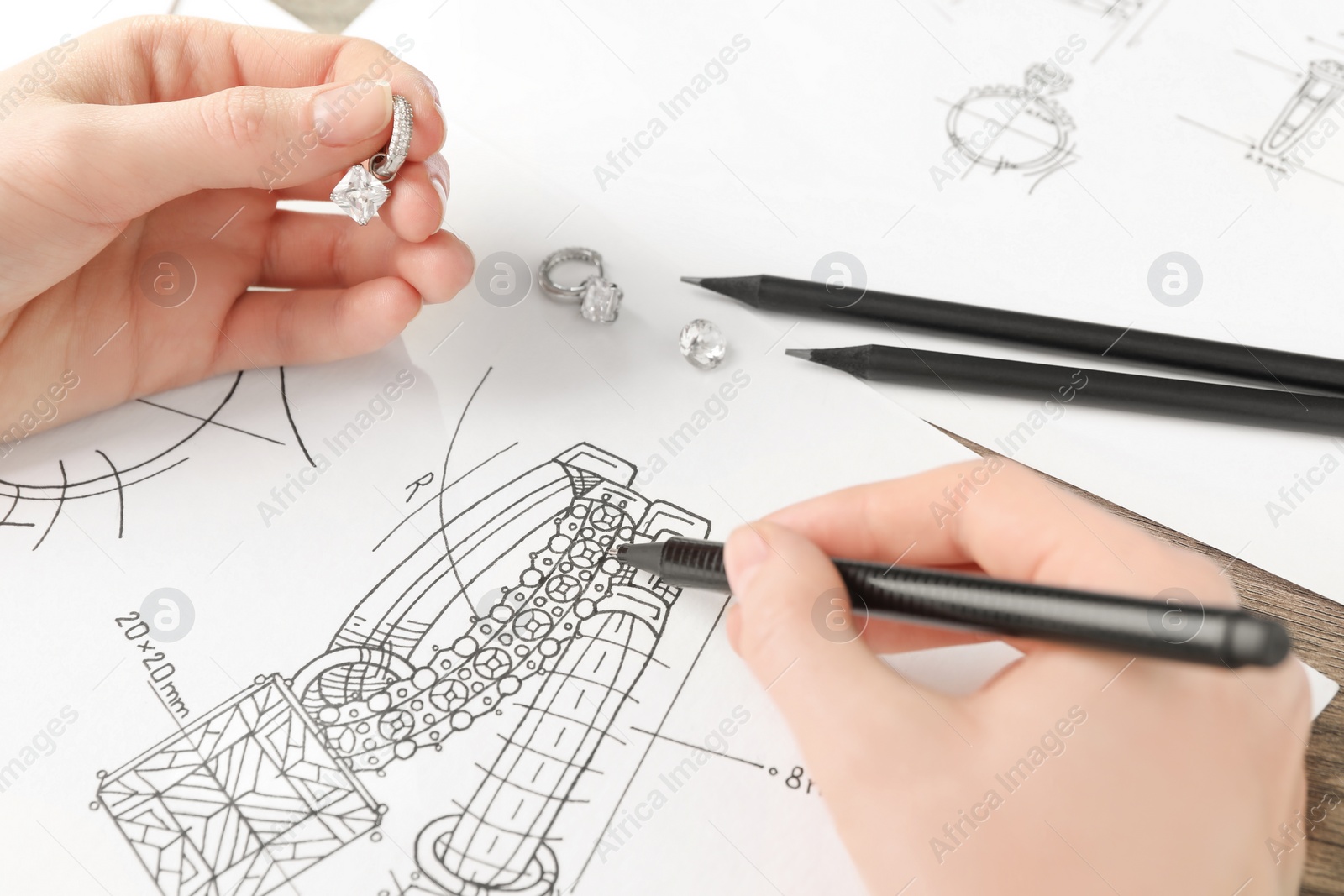 Photo of Jeweler drawing sketch of elegant earrings on paper, closeup