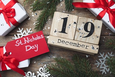 Photo of Saint Nicholas Day. Block calendar with date December 19, festive decor and gift boxes on wooden table, flat lay