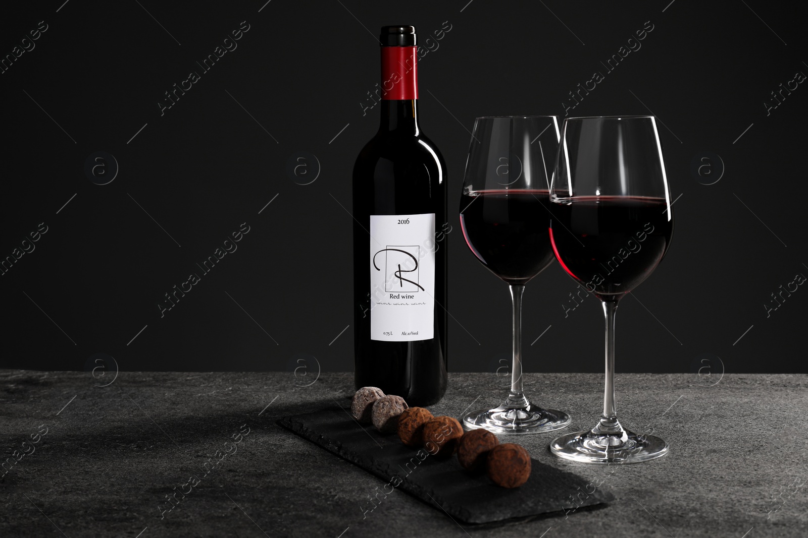 Photo of Red wine and chocolate truffles on gray table against dark background, space for text