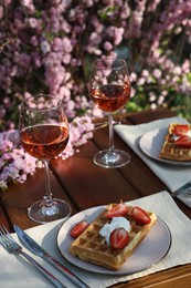 Delicious Belgian waffles with fresh strawberries and wine served on table in garden