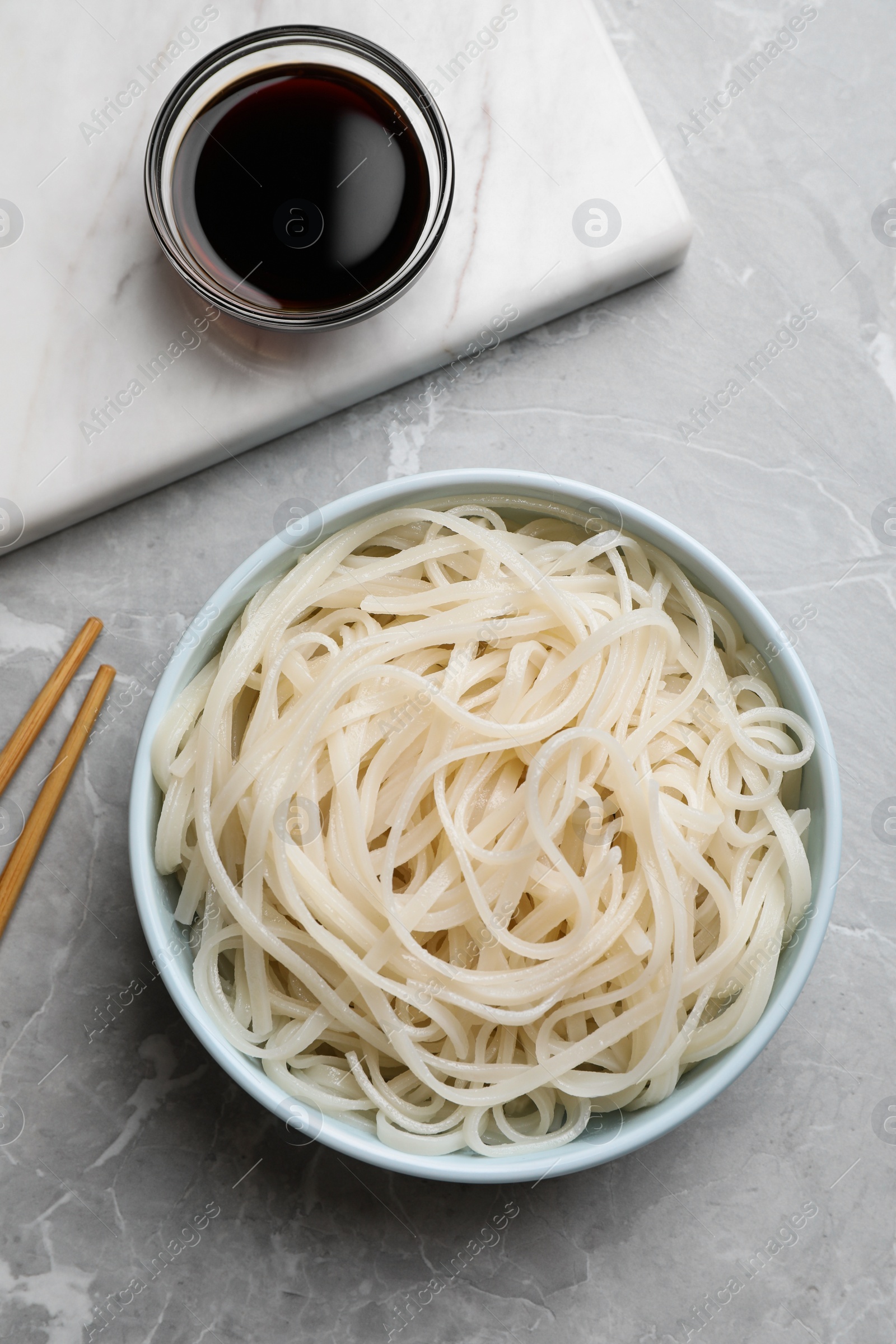 Photo of Bowl of rice cooked noodles and soy sauce served on grey table, flat lay