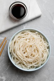 Photo of Bowl of rice cooked noodles and soy sauce served on grey table, flat lay