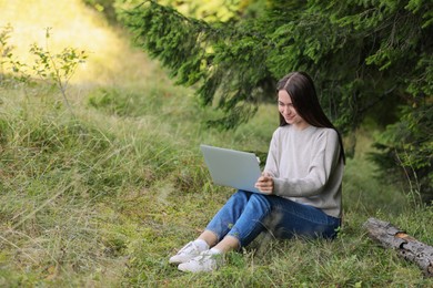 Photo of Young woman working on laptop in forest, space for text
