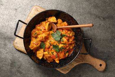 Photo of Delicious chicken curry in frying pan and spoon on grey table, top view