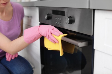 Photo of Woman cleaning oven with rag in kitchen, closeup