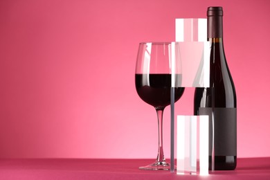 Stylish presentation of delicious red wine in bottle and glass on pink background. Space for text