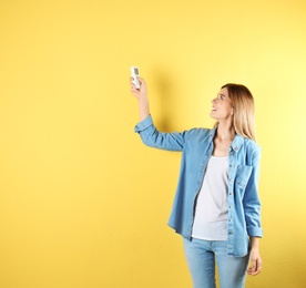 Woman with air conditioner remote on color background