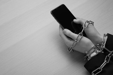 Above view of internet addicted woman with chained hands using smartphone at wooden table, space for text. Black and white effect