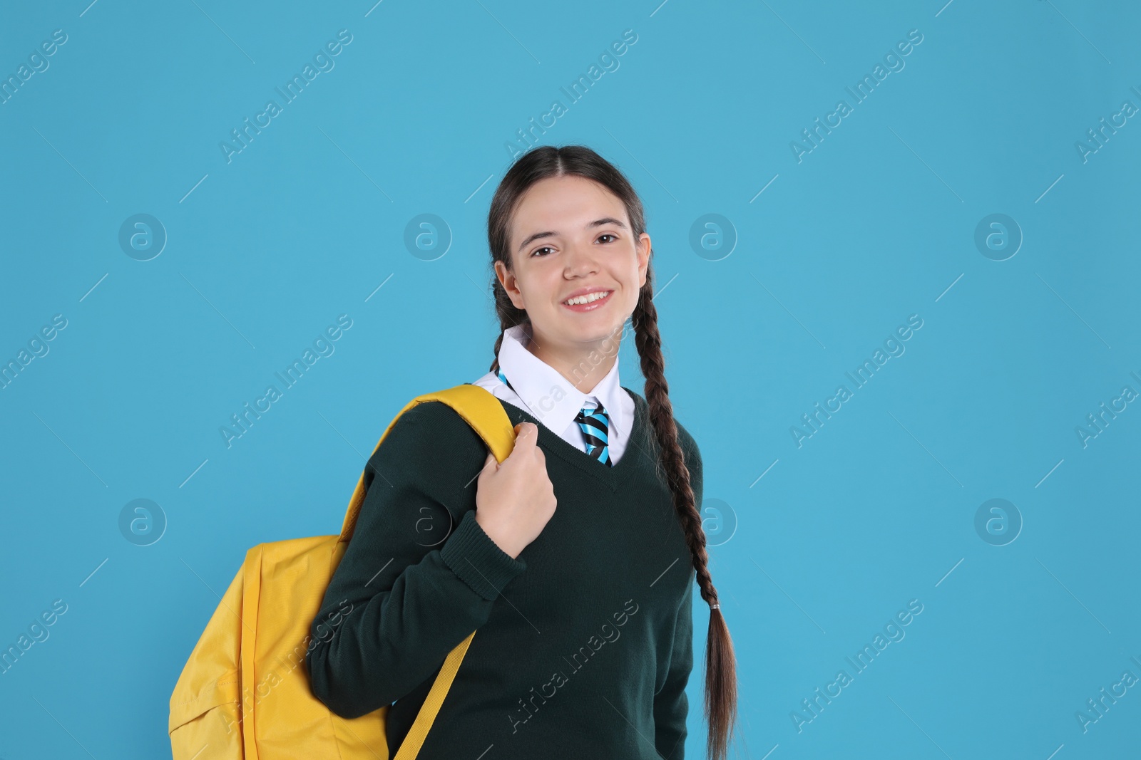 Photo of Teenage girl in school uniform with backpack on light blue background