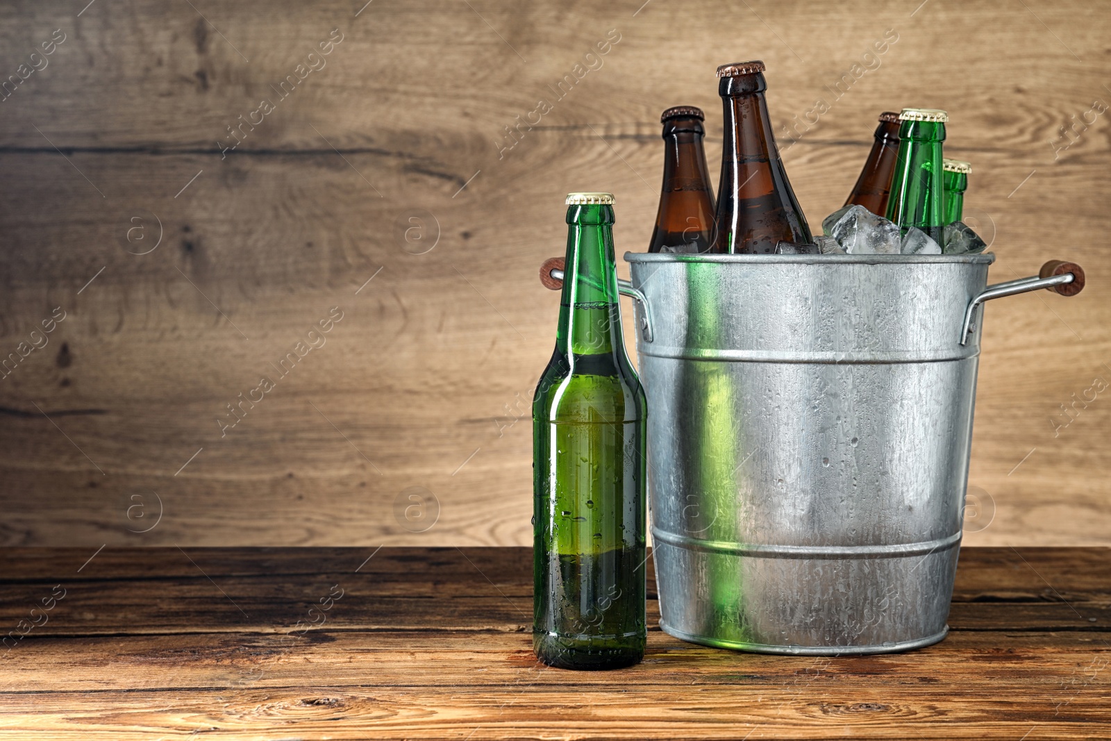 Photo of Metal bucket with beer and ice cubes on wooden table. Space for text