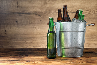 Metal bucket with beer and ice cubes on wooden table. Space for text