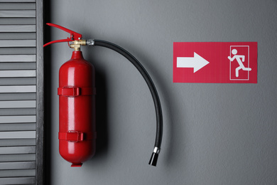Photo of Fire extinguisher and emergency exit sign on grey wall indoors