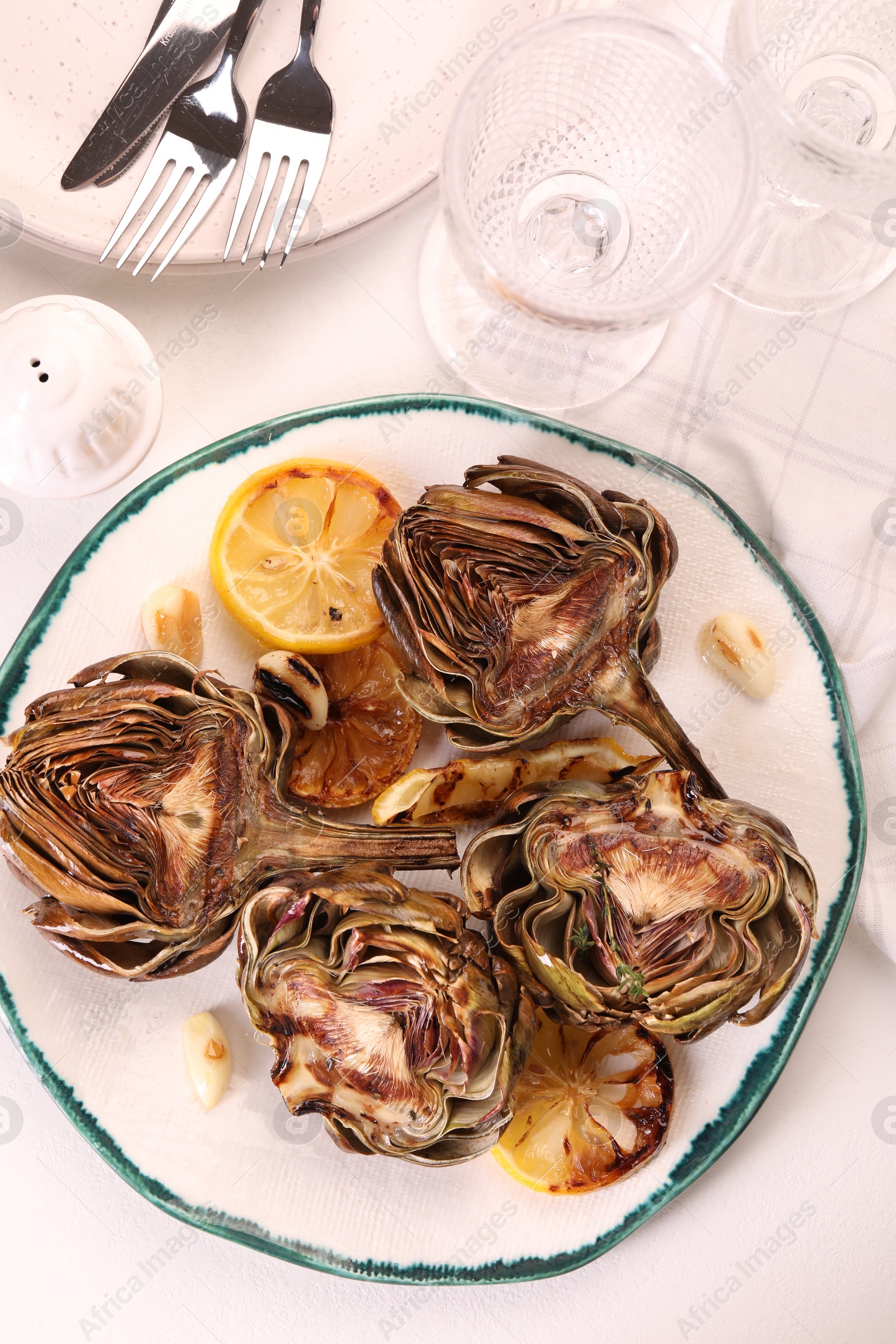 Photo of Plate with tasty grilled artichokes served on white table, flat lay