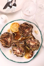 Photo of Plate with tasty grilled artichokes served on white table, flat lay