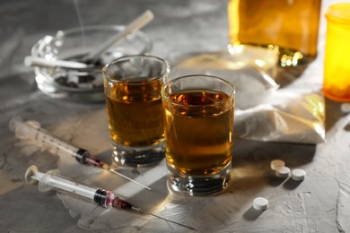 Photo of Alcohol and drug addiction. Whiskey in glasses, syringes, pills and cocaine on grey table