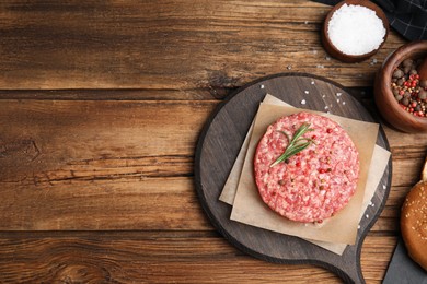 Photo of Raw hamburger patties with rosemary and spices on wooden table, flat lay. Space for text