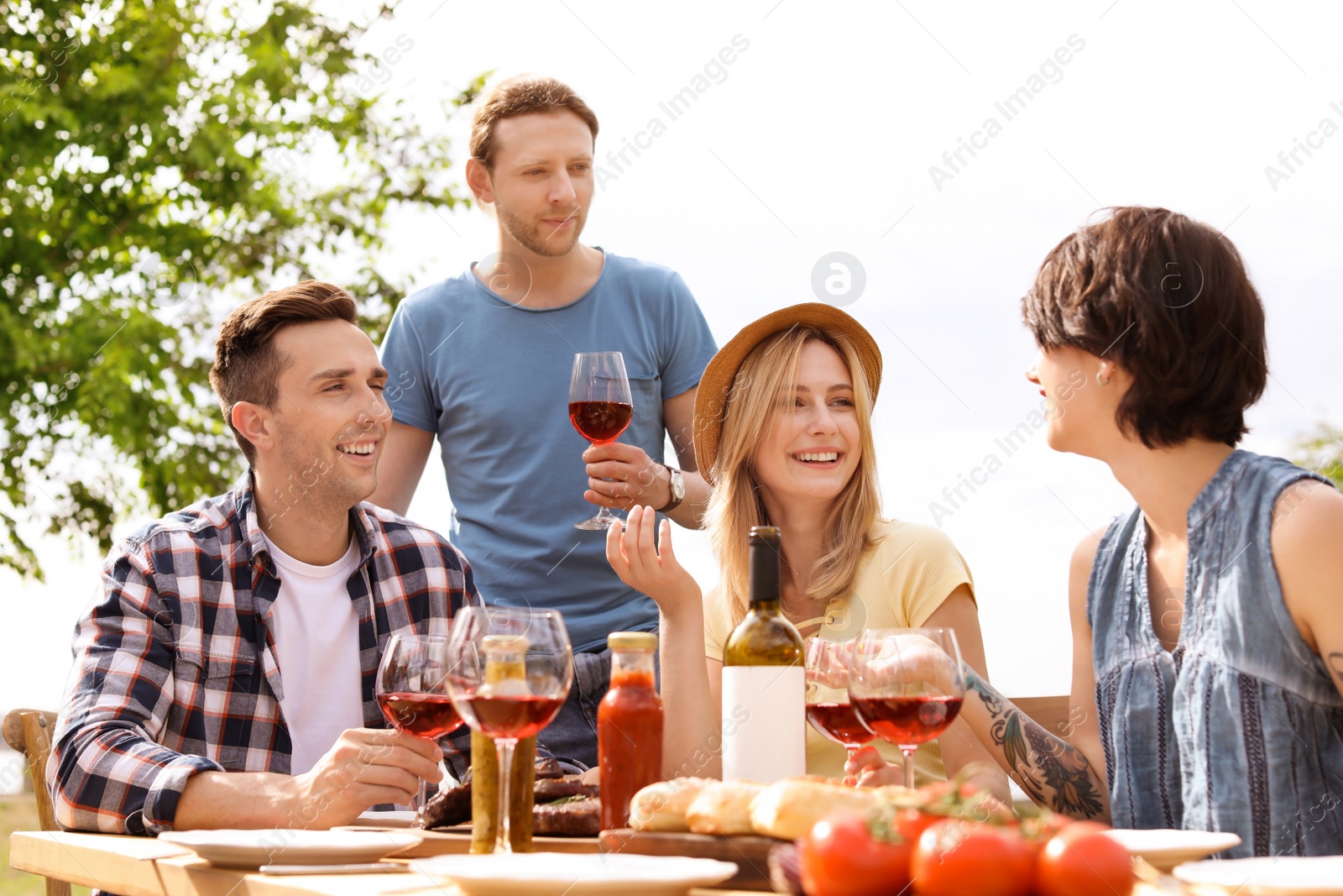 Photo of Young people with glasses of wine at table outdoors. Summer barbecue