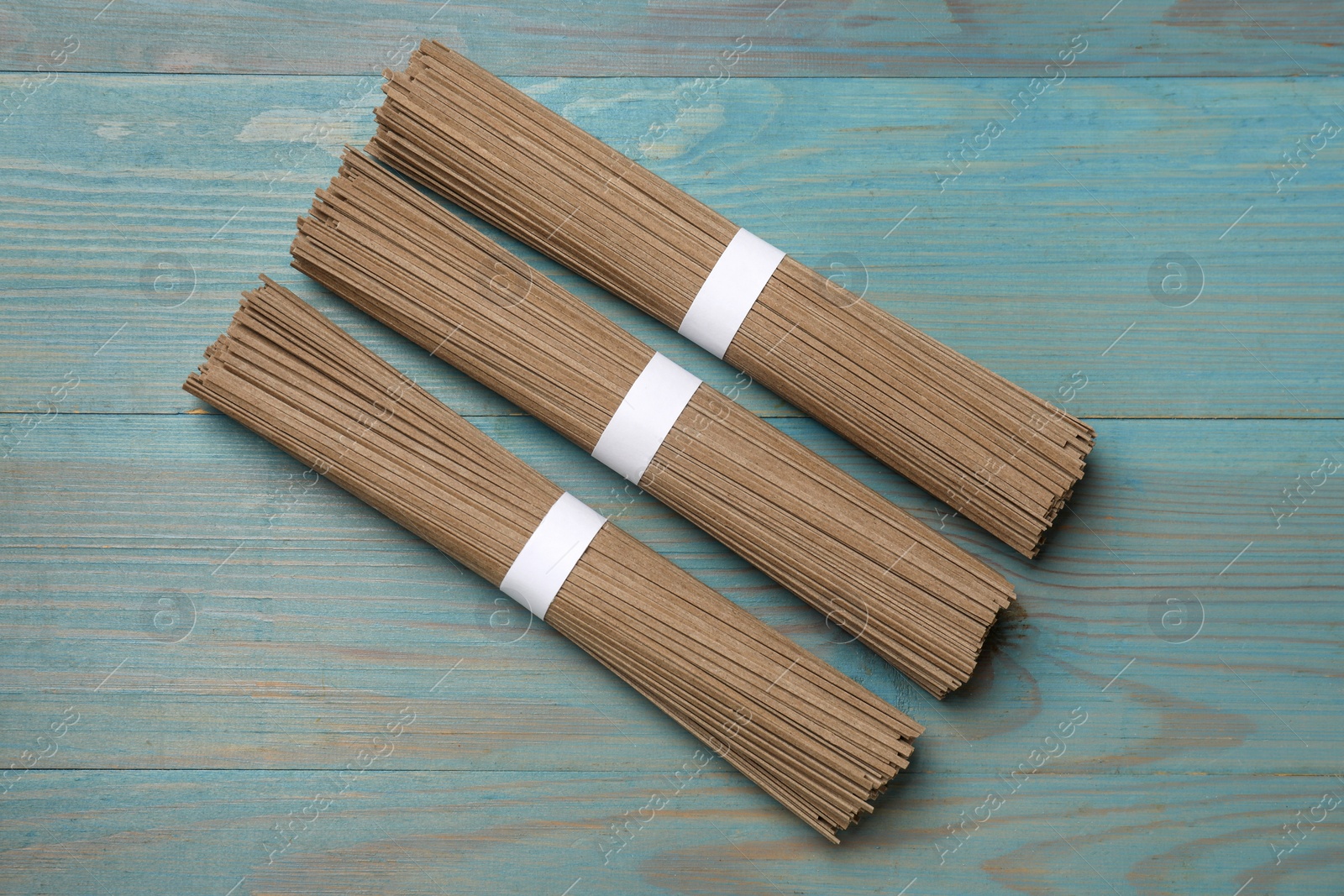 Photo of Uncooked buckwheat noodles (soba) on light blue wooden table, flat lay