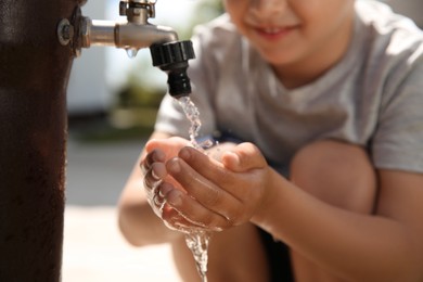 Photo of Water scarcity. Little boy drinking water from tap outdoors, closeup