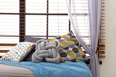 Photo of Plaid and pillows on bed near window indoors. Idea for interior design