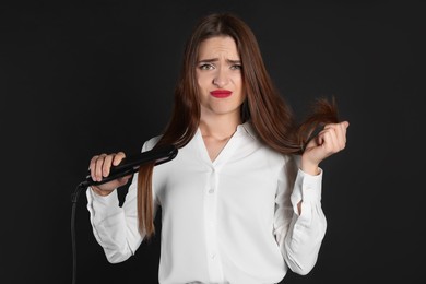 Photo of Stressed young woman with flattening iron on black background. Hair damage