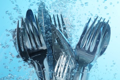 Photo of Washing silver cutlery in water on light blue background