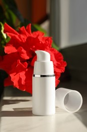 Photo of Bottle of face cream and flowers on white table indoors