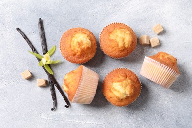 Photo of Delicious sweet muffins, vanilla pods and brown sugar on light grey textured table, flat lay